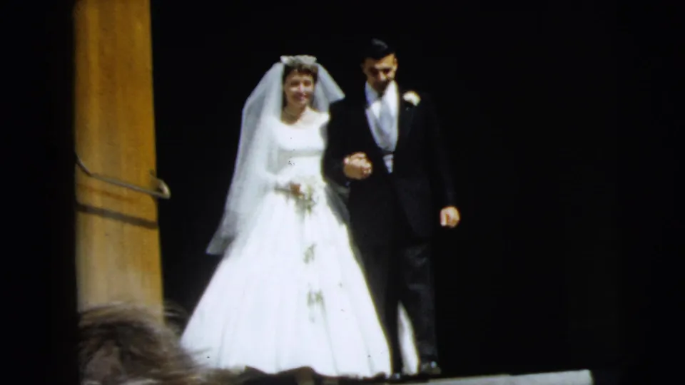 The bride and groom continue down the steps arm-in-arm, with the bride holding a bouquet and the groom wearing a boutonniere.