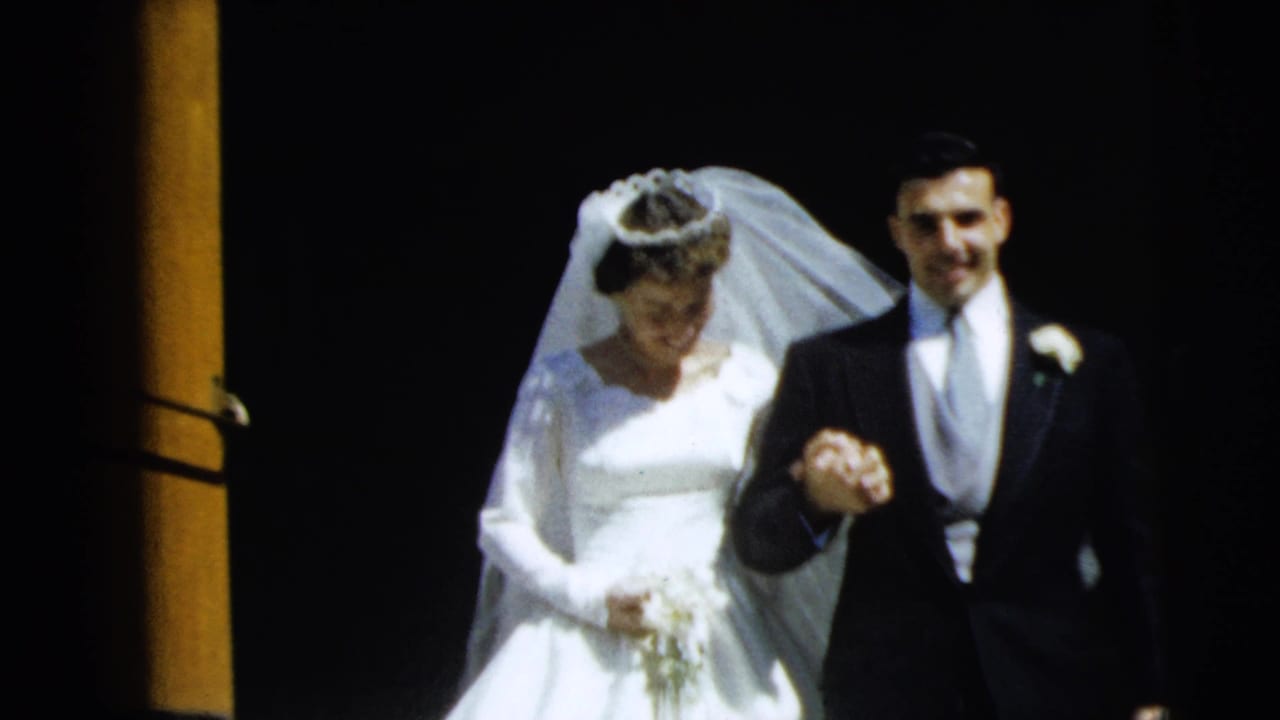Bride and groom walking from a dark church doorway, holding hands in bright sunlight.