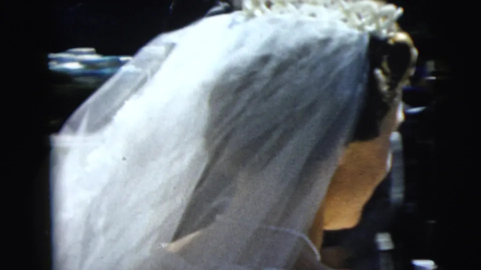 Side view of the bride's veil and floral headpiece during the Camden wedding departure, with guests partly visible behind her.
