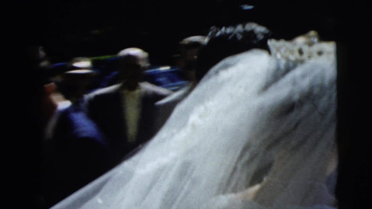 In 1962 Camden wedding footage, the bride's long veil fills the frame while several guests stand in the shaded background.