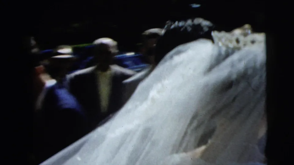 In 1962 Camden wedding footage, the bride's long veil fills the frame while several guests stand in the shaded background.