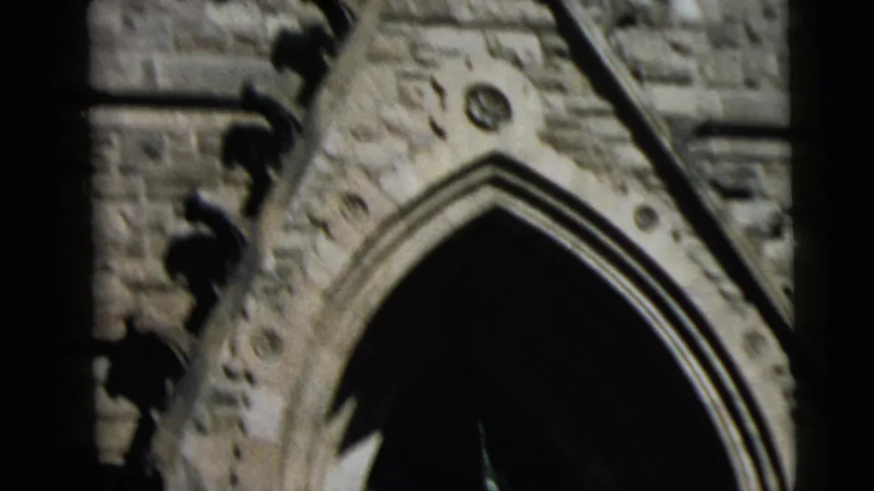 Low-angle view of the church entrance area, with a pointed arch, carved stonework, and partial facade details in soft 8mm focus.