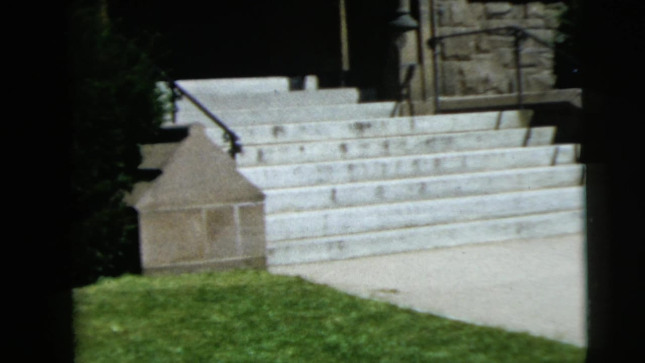 Stone church steps with grass, railing, and part of the entrance in sunlight.