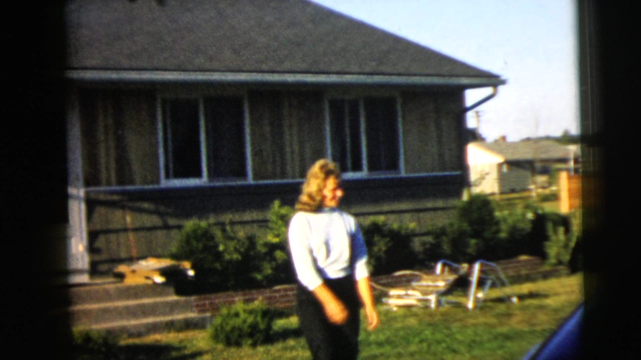 In the Camden backyard, the woman lowers her hands and turns, with lawn chairs and the house behind her.