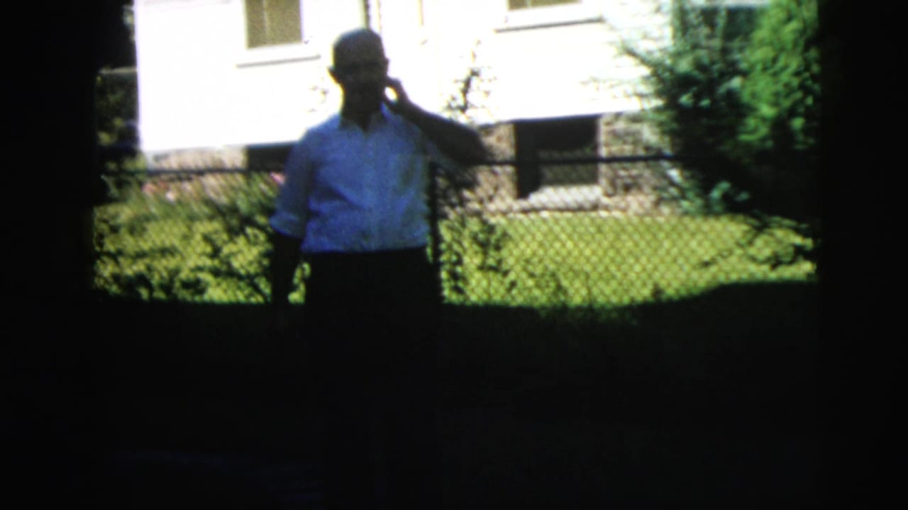The Camden 1962 exterior view repeats with the man silhouetted in partial shade as he holds the phone near a residential lawn.