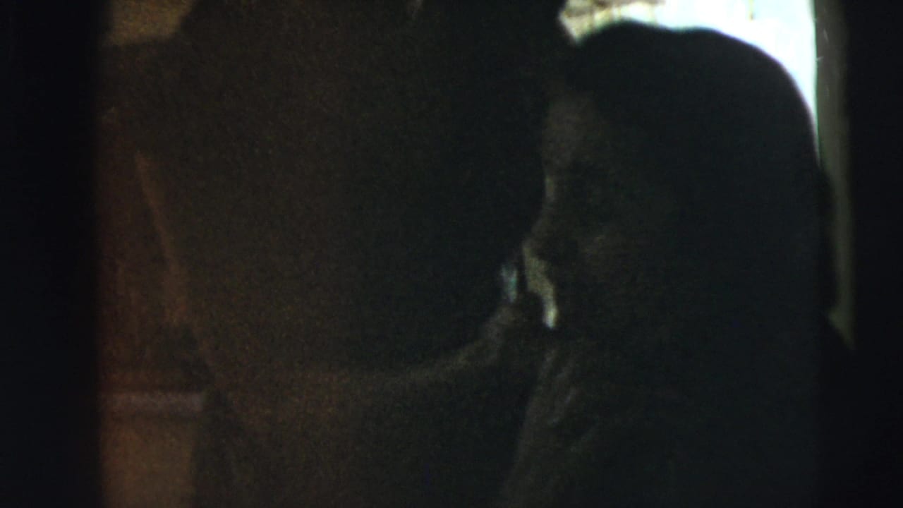 Dark interior with silhouetted figures near a bright window.