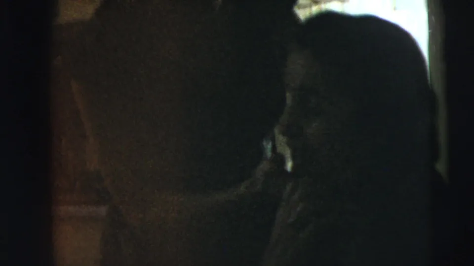 1962 Camden home-movie frame showing shadowed figures in a dim interior near a bright window opening.