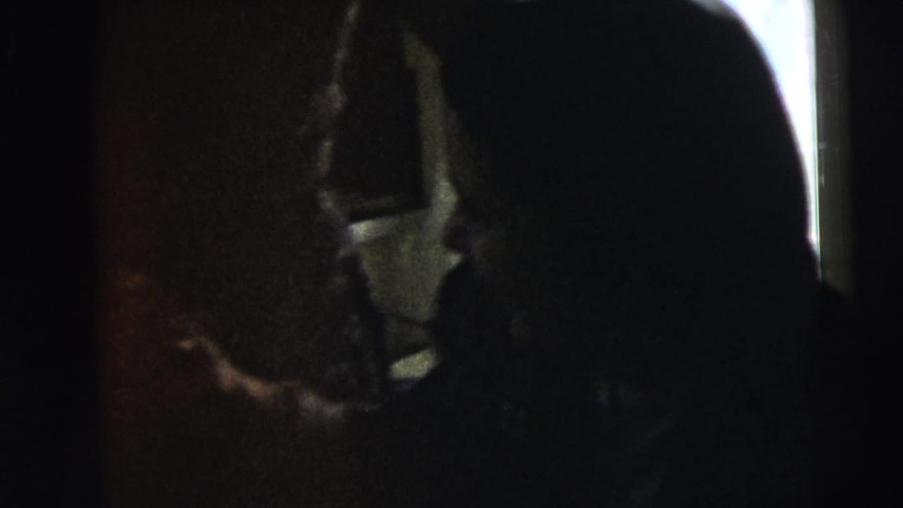 Two dark silhouettes face each other in a dim room by a window.