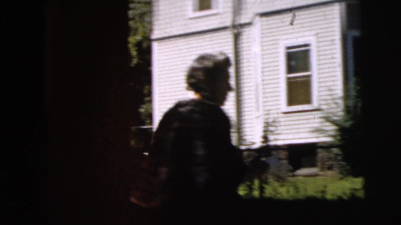 Two figures are partly obscured by dark vertical film or camera framing outdoors.