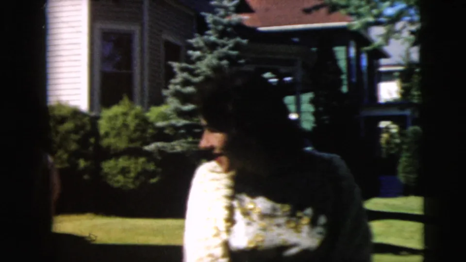 A shadowed figure stands near the lawn and shrubs outside a Camden residential house in 1962 footage.