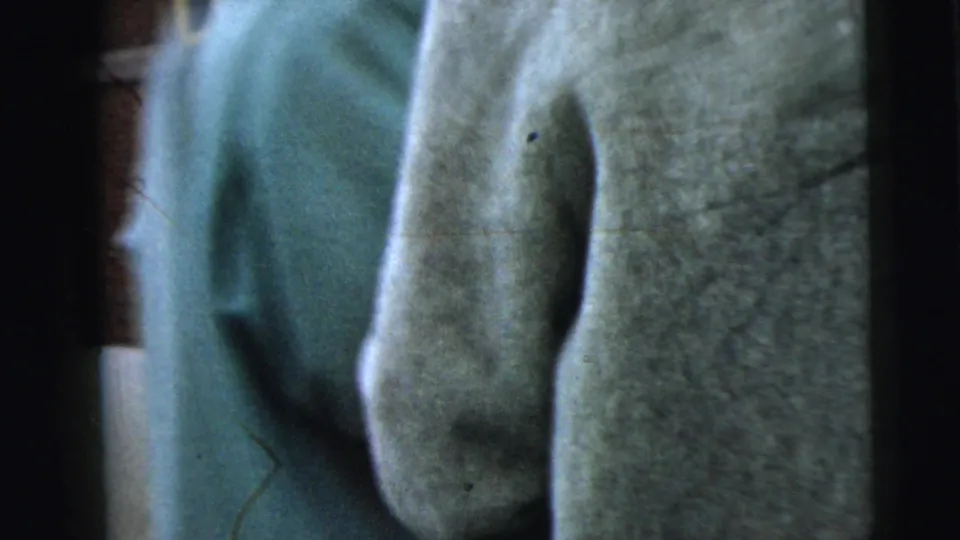 Soft 8mm close-up of light fabric filling the frame, with visible grain, dust marks, and a partial blue garment nearby.