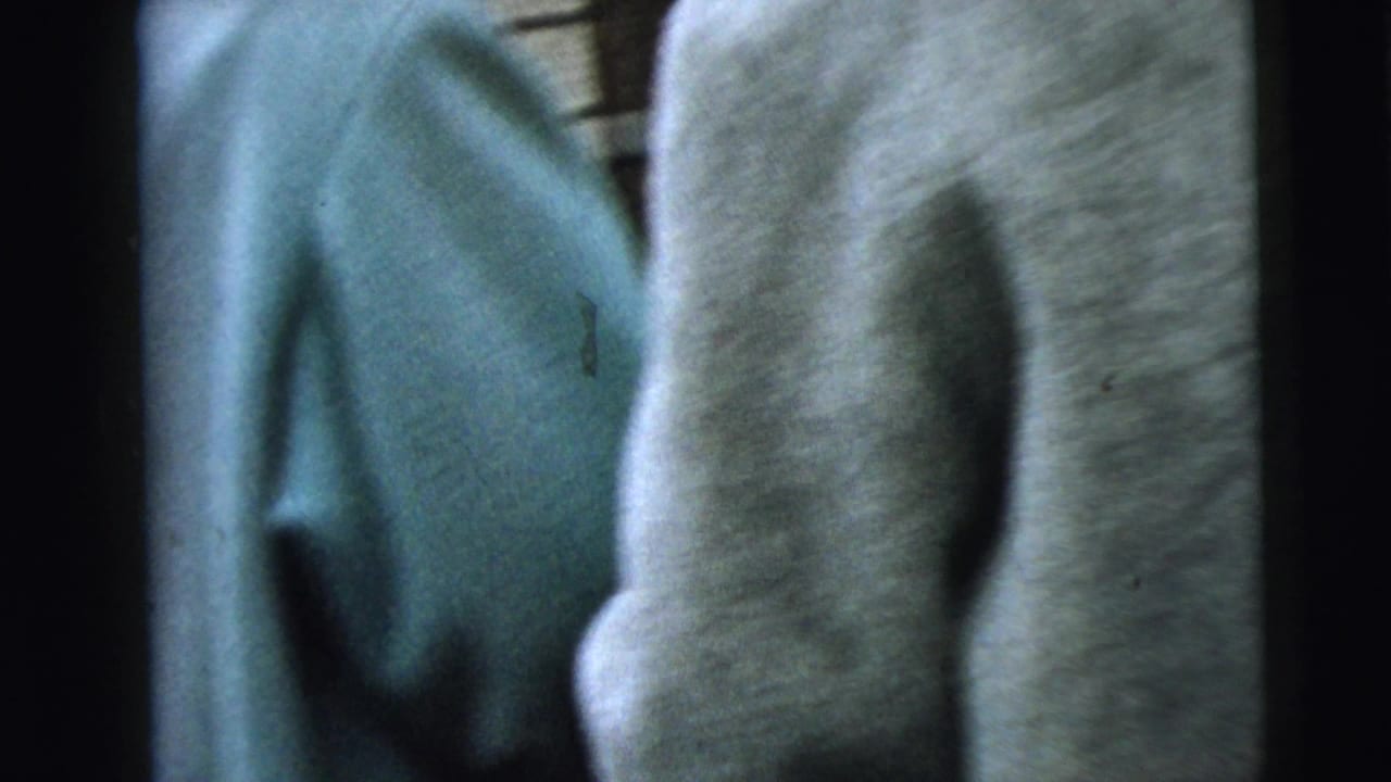 Two women in blue and gray coats seen from behind while walking near a brick building.