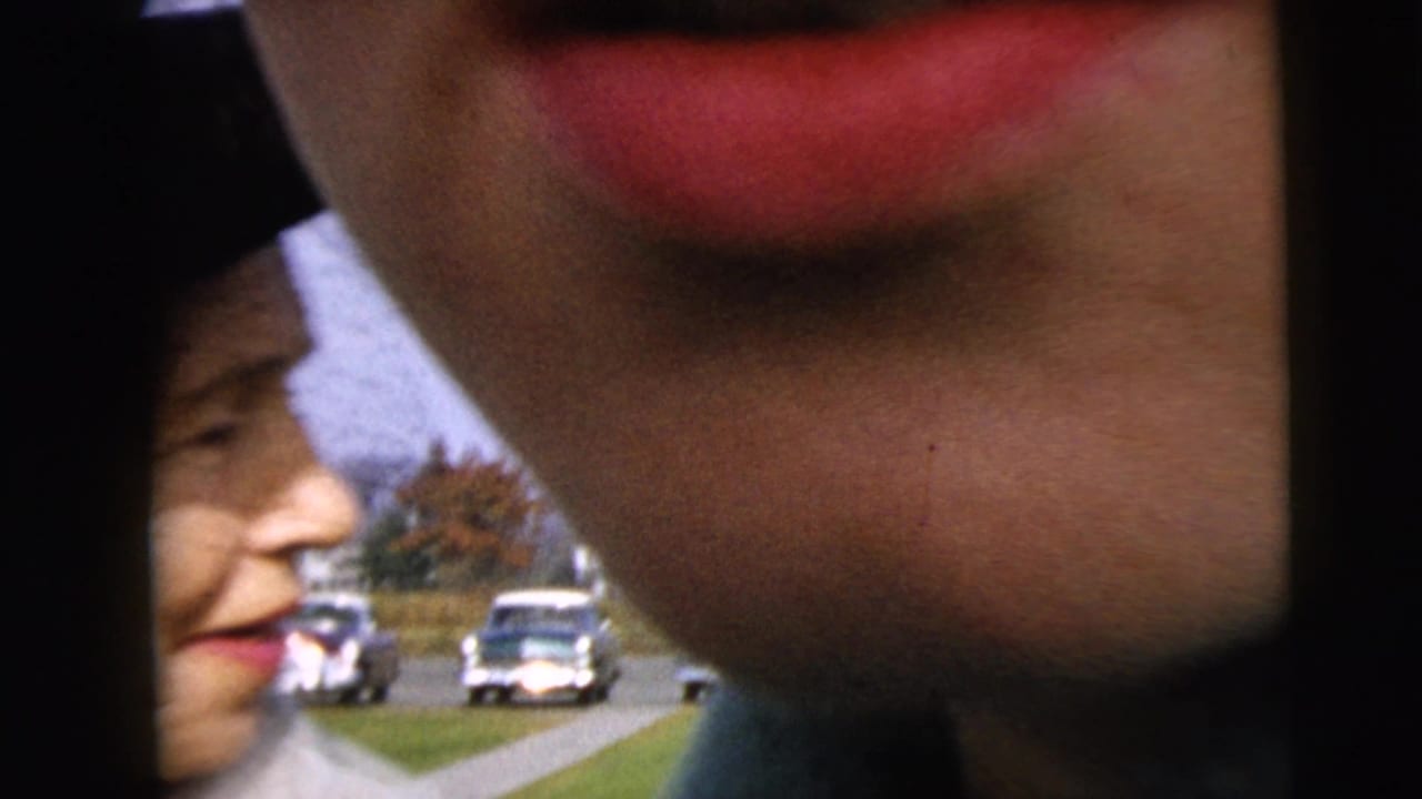 Close handheld 8mm view of people near a street or parking area in Camden, New Jersey, with mid-century cars and grass behind them.