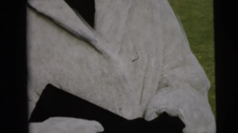 Close view of a light-colored long coat in the 1962 Camden home-movie footage, framed tightly as the person passes the camera.