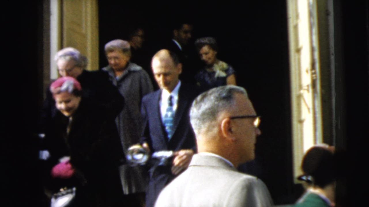 In Camden, New Jersey in 1962, formally dressed adults leave a building while onlookers and suited men stand near the entrance.