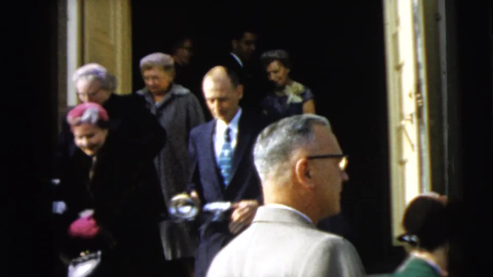In Camden, New Jersey in 1962, formally dressed adults leave a building while onlookers and suited men stand near the entrance.