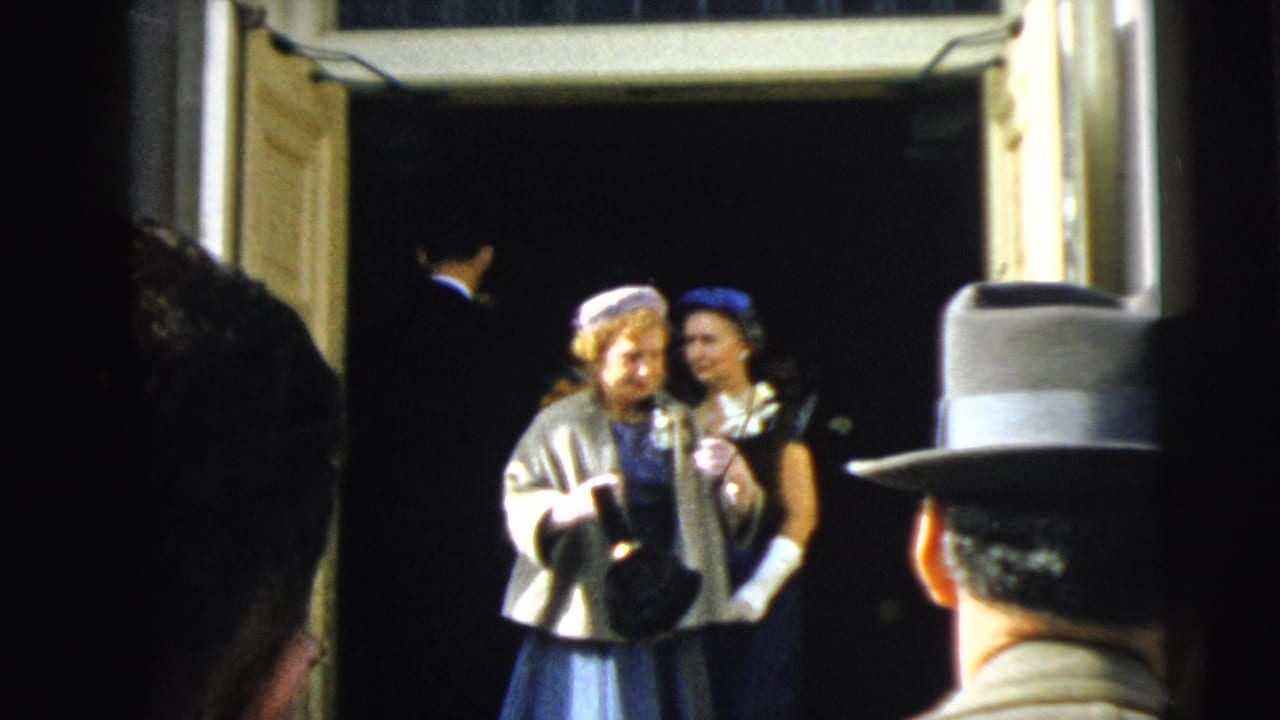 Two women in 1960s formal wedding attire pause in the open doorway, with a man in a suit partly seen behind them.