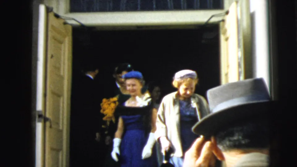 The wedding party begins to move outward through the open doors, with women in hats and gloves leading the exit.