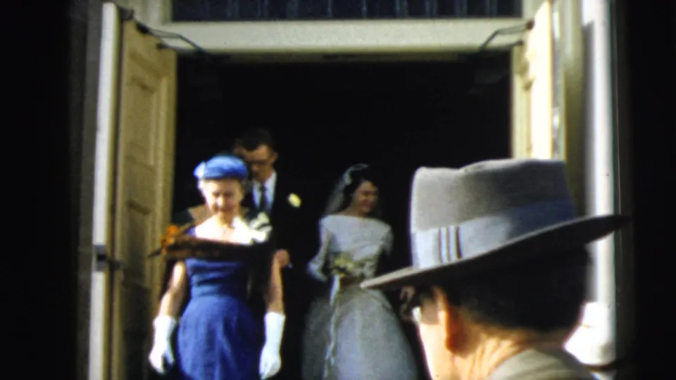 The bride in a white gown and veil emerges last behind the wedding party, holding a bouquet in the Camden doorway scene.