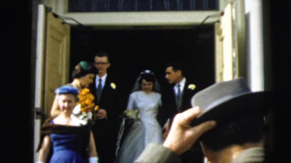 In Camden, New Jersey in 1962, a bride and groom step from a church doorway with wedding attendants and guests in period dress.