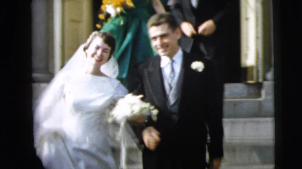 A smiling bride and groom walk arm-in-arm down the church steps during their 1962 Camden wedding exit.