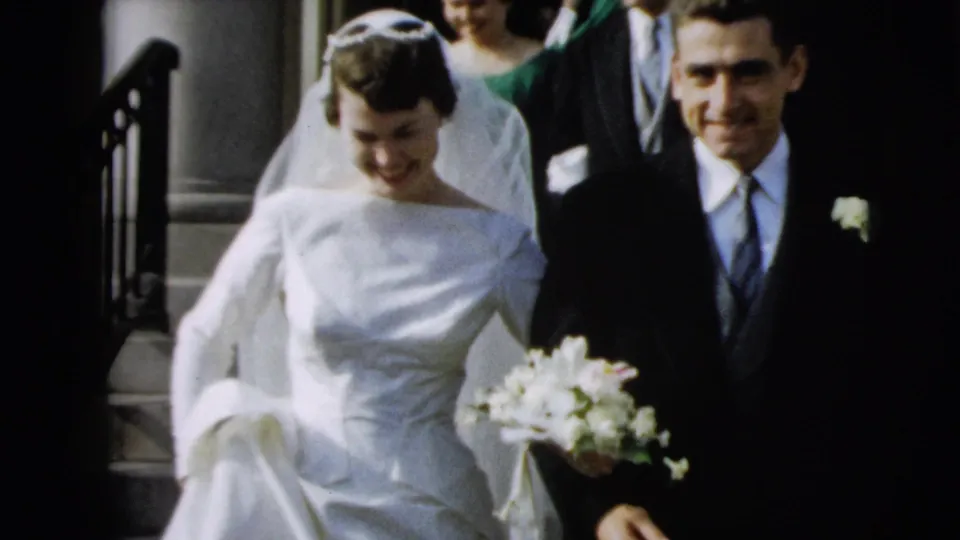The bride looks down while stepping carefully beside the groom, bouquet visible, during the Camden church wedding exit.