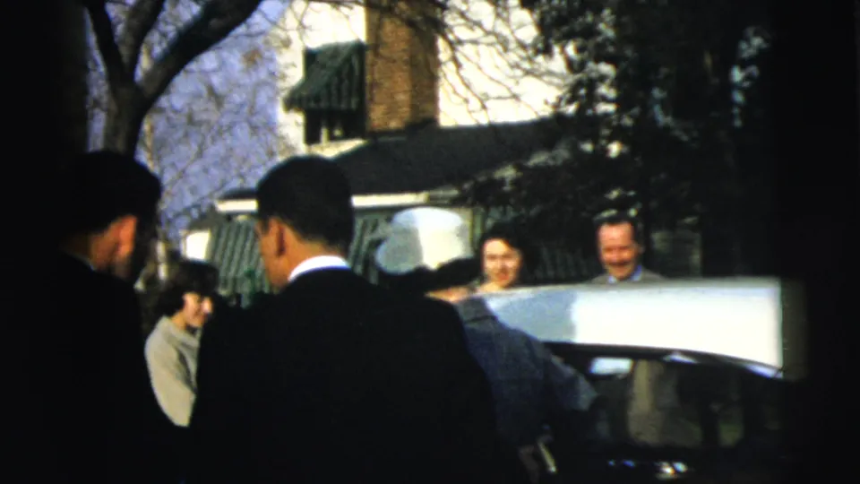 Wedding guests in formal clothing gather around a car door in the Camden residential setting noted by the clip metadata.