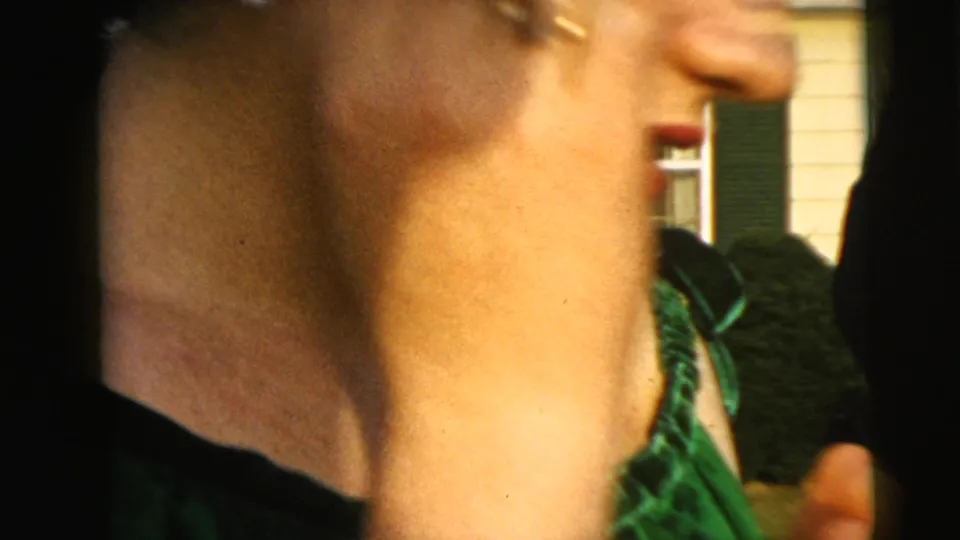 1962 Camden home-movie frame showing a close partial profile of a woman in a shiny green ruffled dress outdoors.