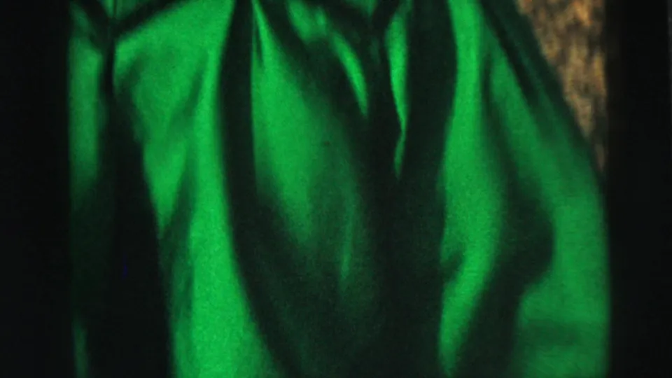 Close 8mm frame of the bright green ruffled dress fabric catching sunlight as the woman moves outdoors.