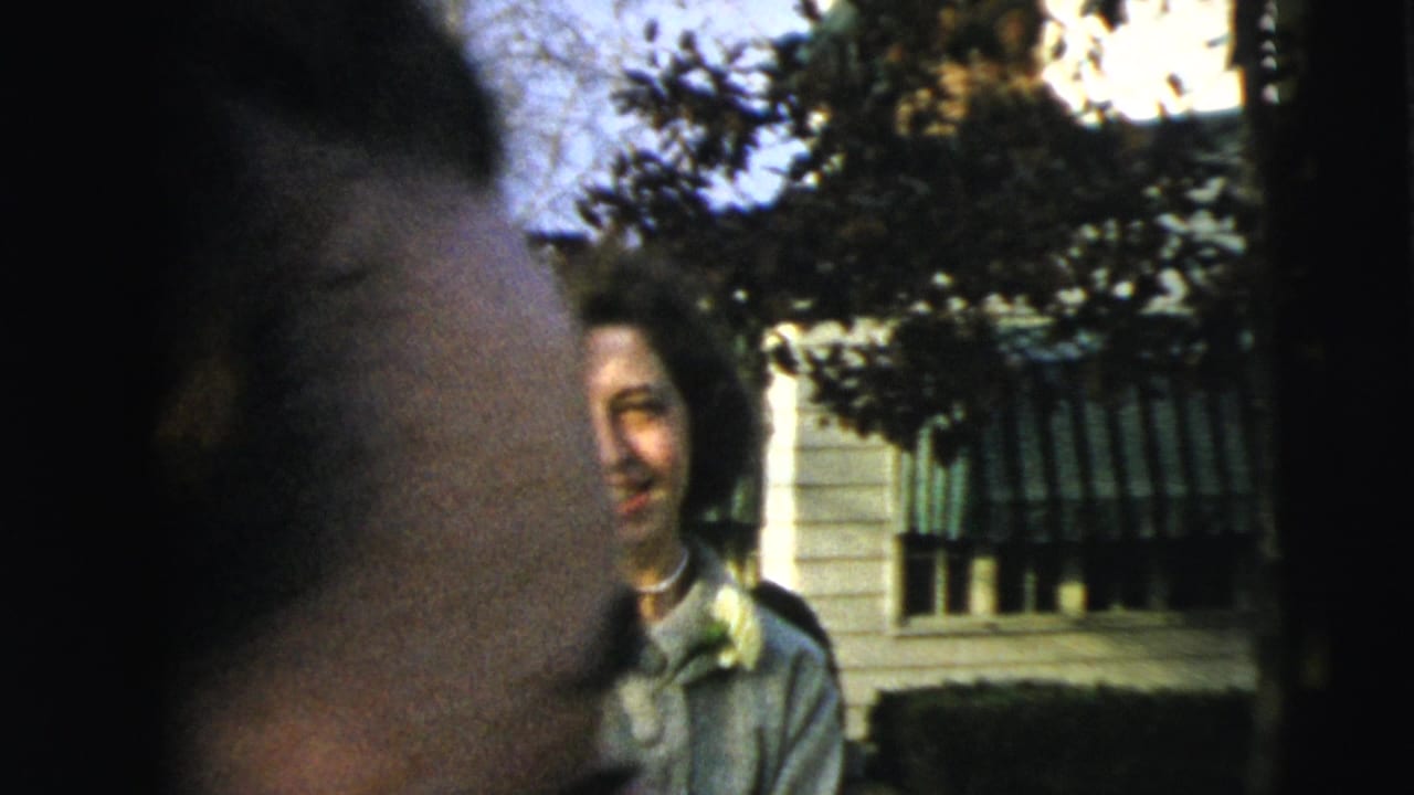 In Camden, New Jersey, a woman passes close to the camera while another woman stands smiling near a house in 1962 home-movie footage.