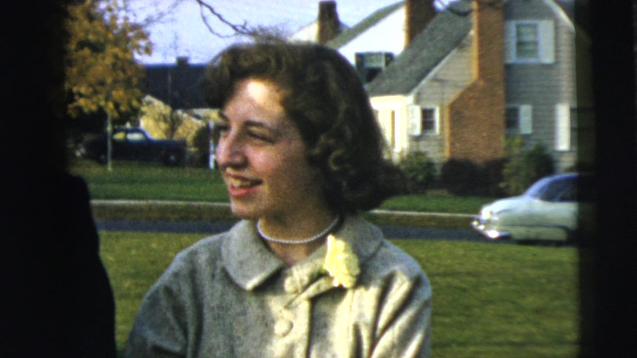In Camden, New Jersey 1962 footage, a smiling woman in a light dress stands outdoors with houses, lawn, and a car behind her.