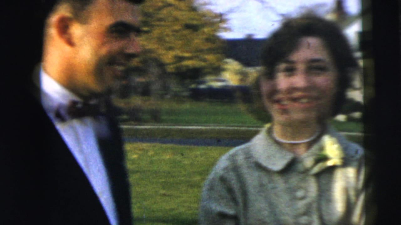 A groom in a dark suit and bow tie stands beside the woman with a corsage in Camden, New Jersey 1962 home-movie footage.