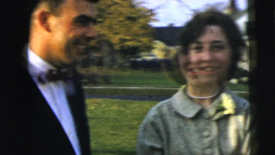 A groom in a dark suit and bow tie stands beside the woman with a corsage in Camden, New Jersey 1962 home-movie footage.