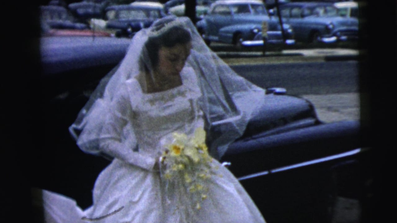 The bride, wearing a long veil and white gown, holds a yellow-and-white bouquet beside a dark limousine in Camden, New Jersey, 1962.