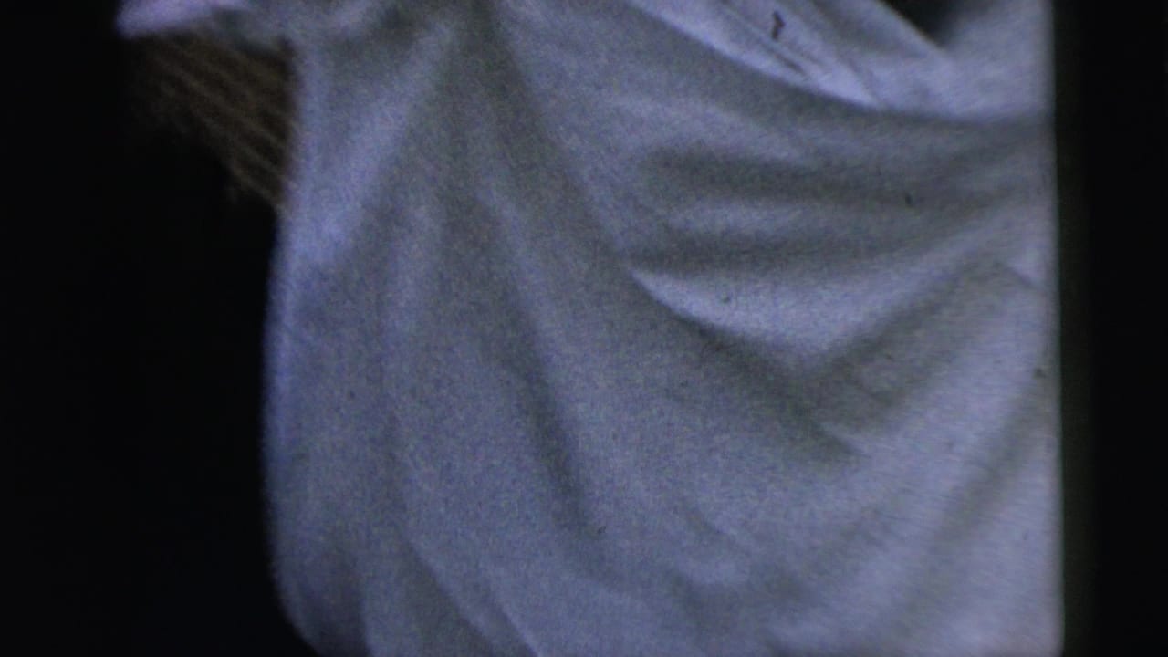 Soft, close cropped 8mm frame showing pale fabric, possibly a dress or coat, with dark film-edge shadows around it.