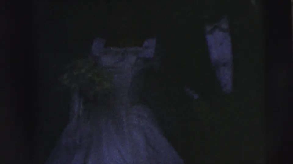 Dark 8mm frame showing a formal white gown and a nearby tuxedoed figure, suggesting an evening or special occasion moment.