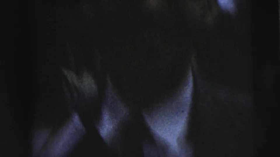Very dark 8mm frame from the Camden clip with a close-up of an adult face, shirt collar, and jacket edge.
