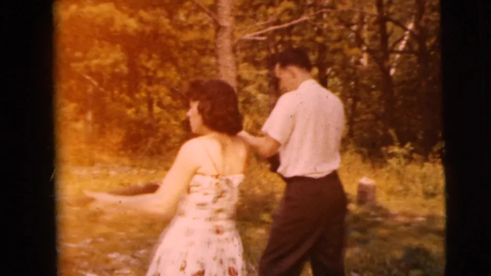 1962 Camden 8mm frame showing a woman in a light floral dress beside a man in a white shirt holding a long gun outdoors.