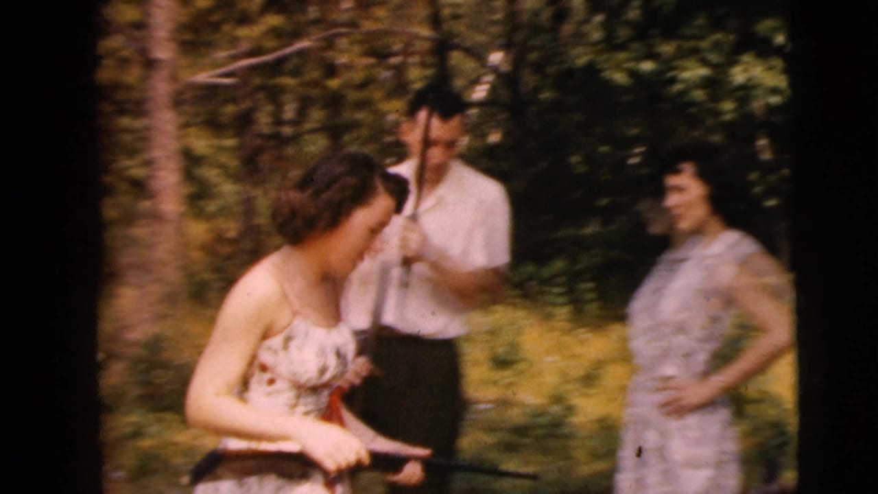 A Camden, New Jersey 1962 home-movie frame shows two women and a man outdoors as a rifle is handled in a wooded clearing.