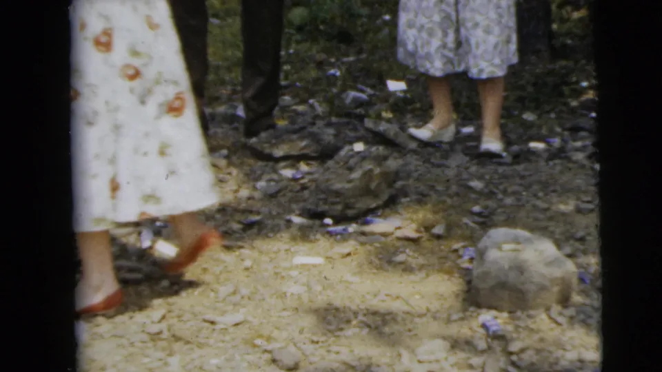 The final frame shows adult legs, dresses, shoes, dirt, stones, and a wooded edge in the supported 1962 Camden-area home movie.
