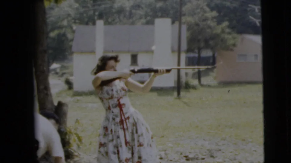 In Camden, New Jersey, 1962 home-movie footage, a woman in a floral dress aims a rifle across a backyard with trees and houses beyond.