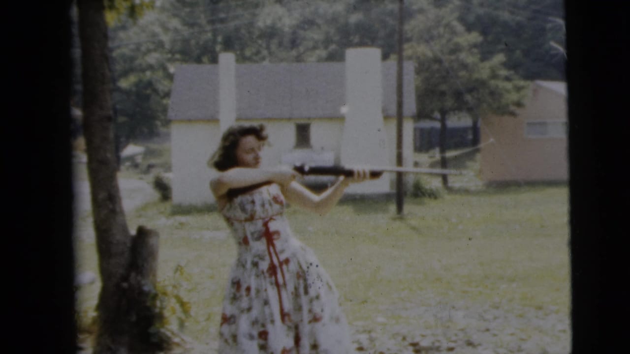 A woman in a floral dress keeps a rifle raised in a Camden backyard scene dated 1962, with houses and trees in the background.