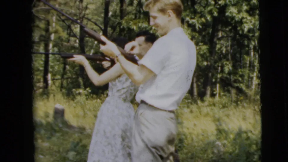 Near Camden, New Jersey, a man in a white shirt holds a rifle while a woman beside him aims another rifle in the sunlit woods.