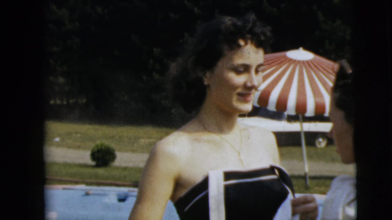 The woman stands by the pool in Camden, New Jersey, facing a partially visible person beside a red and white striped umbrella.