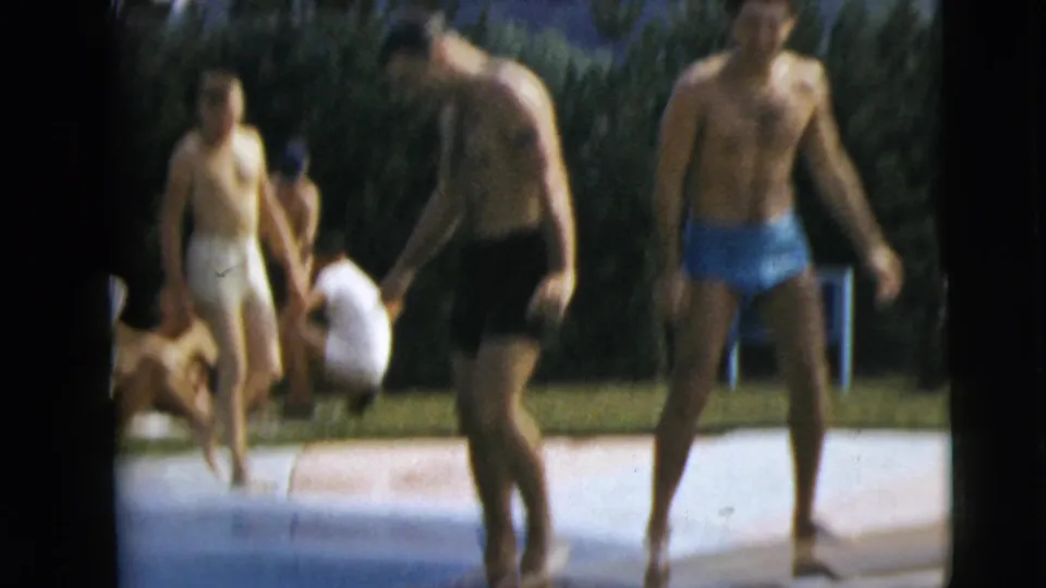 1962 Camden, New Jersey poolside frame with several adult men in swim trunks moving around the pool edge and lawn.