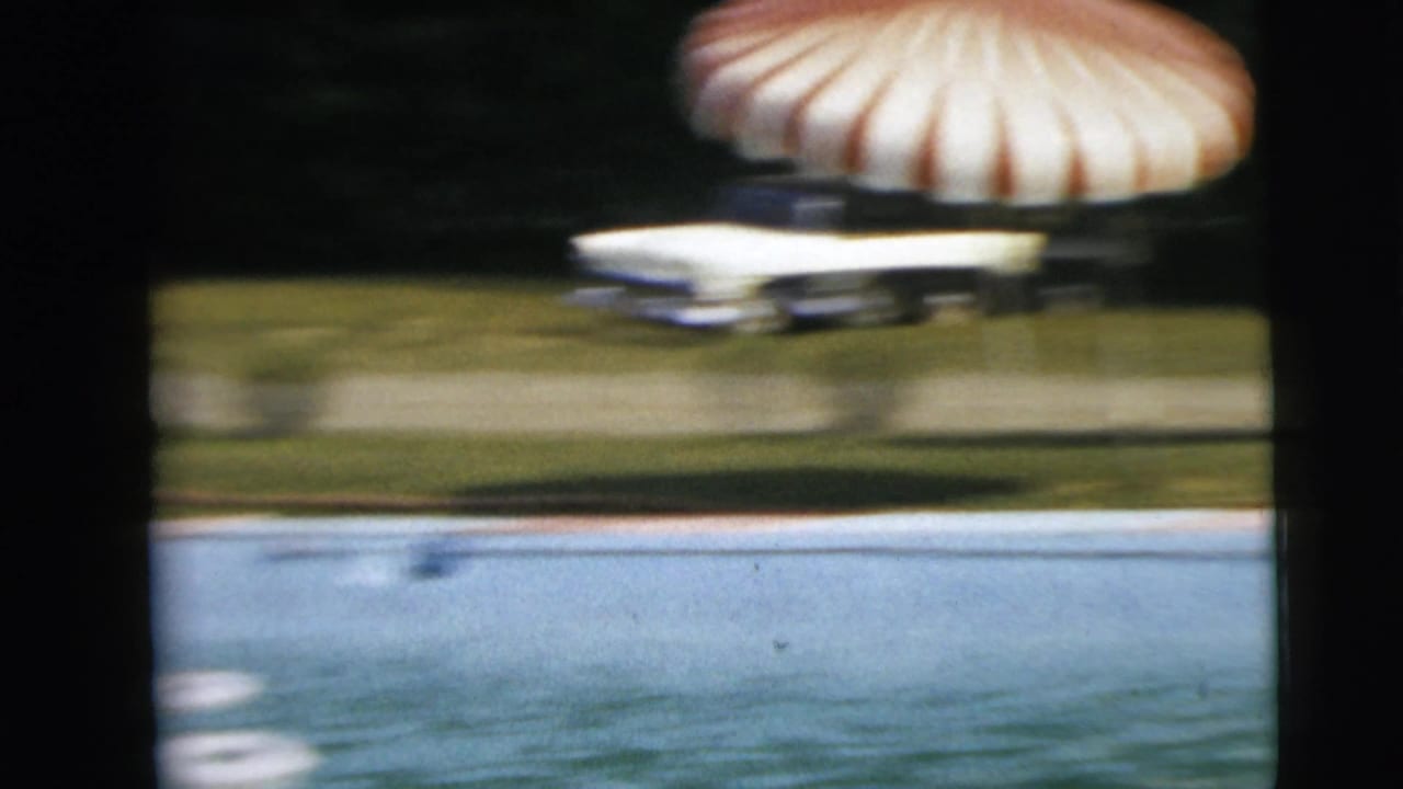 Pool water and lawn with a striped umbrella and a blue-and-white car in the background.