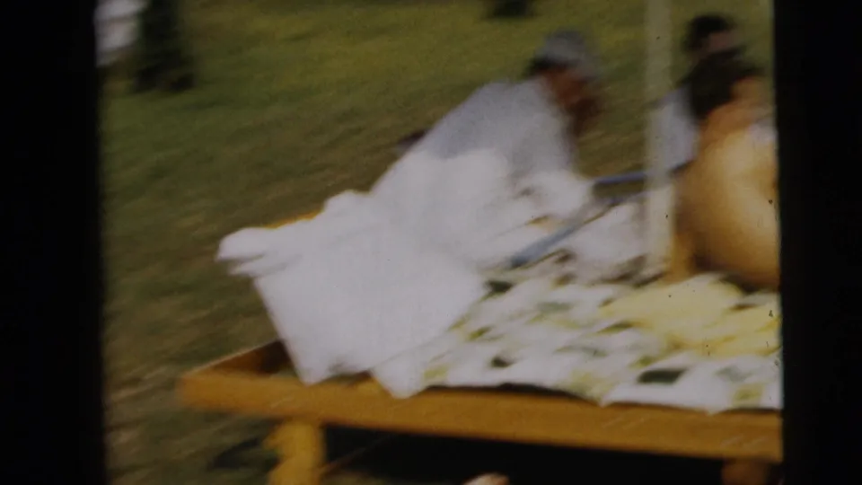 Soft 8mm frame of a poolside lawn scene with a reclining person on a lounge chair and others gathered nearby.