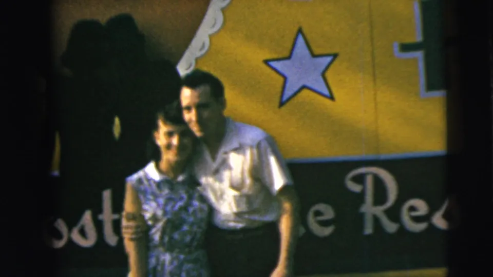A smiling couple poses together in front of a yellow-and-black sign with a star graphic in Camden, New Jersey, according to the 1962 clip metadata.