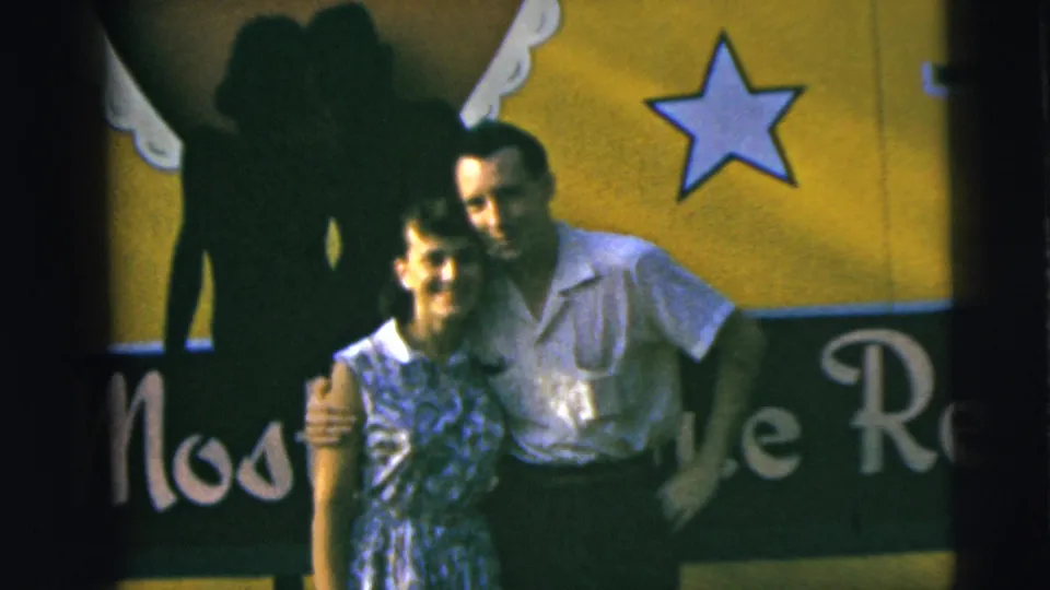A man embraces a woman while they pose in front of a yellow sign with a star and partial lettering, matching the supplied 1962 Camden metadata.