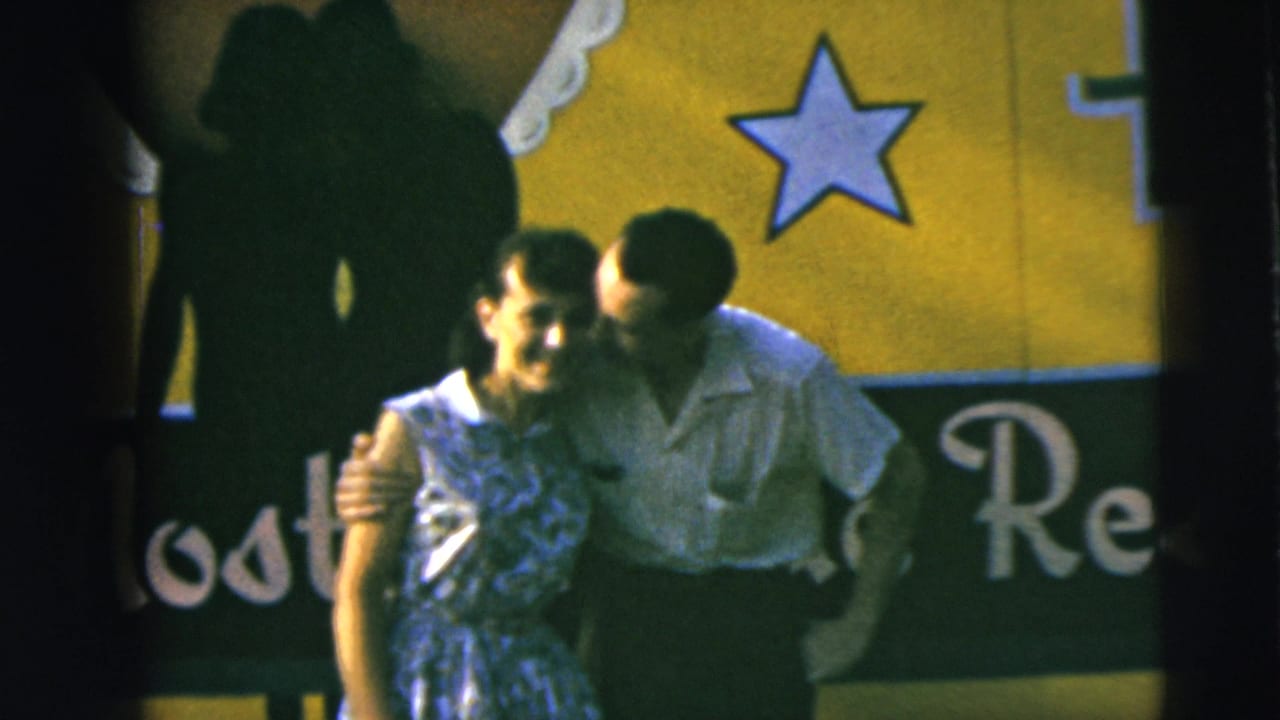 Man kisses or leans toward the woman's cheek while they stand before the sign.
